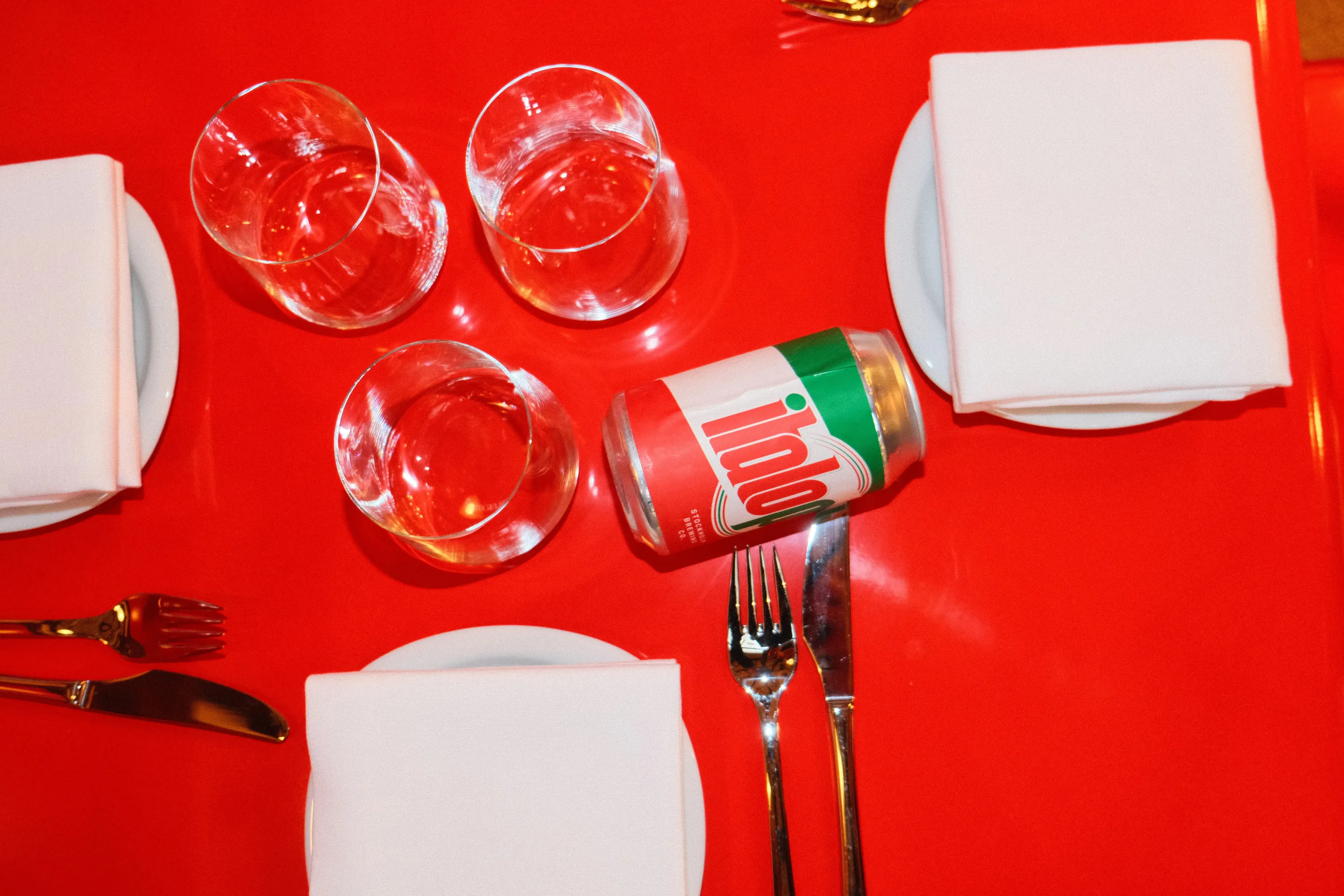 An ItaloPils can among wine glasses on a red table